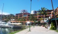 Marina boardwalk with many shops and restaurants with condo buildings on a clear sunny day in Puerto Vallarta.