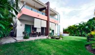 Two story modern style home surrounded by green manicured gardens on a sunny day, an example of Puerto Vallarta homes for sale by owner.