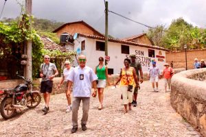 Tour guide and International tourists walking down the street in the town of ¨San Sebastian of the West¨, buildings painted in white with red tile roofs.